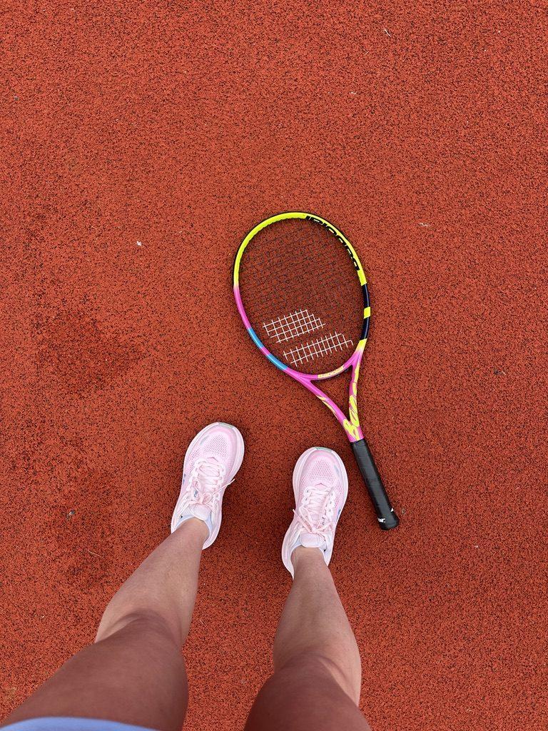 Poppy's trainers and tennis racket on a clay court